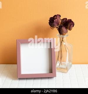 Blank picture frame and red dry rose on white table. orange wall background. copy space Stock Photo