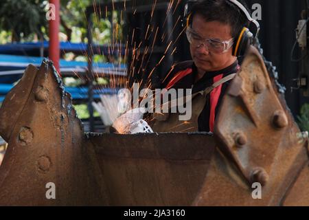 Man work in home workshop with angle grinder, goggles and construction gloves. Sanding metal makes sparks, closeup Stock Photo