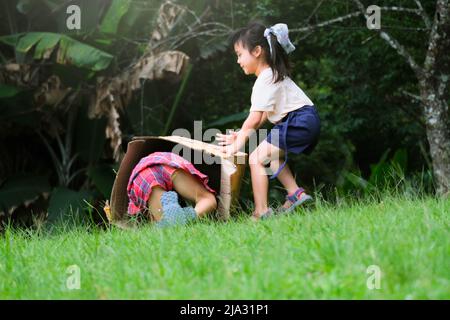 Smiling little girl sits on a cardboard box sliding down a hill at a botanical garden. The famous outdoor learning center of Mae Moh Mine Park, Lampan Stock Photo