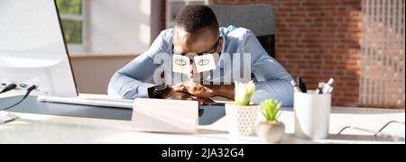 Young Man Covering His Eyes With Adhesive Notes On Desk In Office Stock Photo