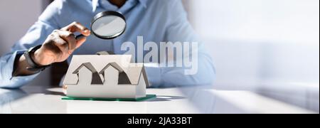 Human Hand Holding Magnifying Glass Looking House Model Over White Desk Stock Photo