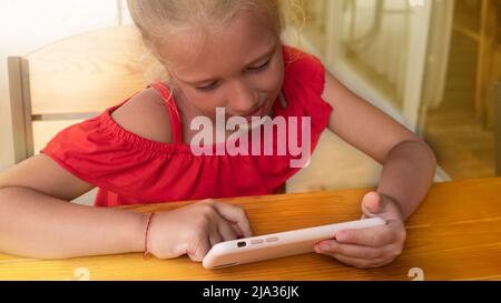 Cute baby girl playing studying using smartphone. A close-up of a tanned and peeling face from the sun.  Bright clothes sunbeam Stock Photo
