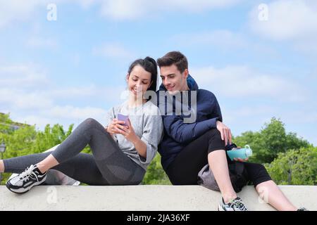 Happy young sport couple checking at the smartphone while sitting at a park. Stock Photo