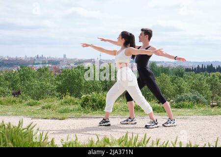 Young couple doing warrior two yoga pose in a park. Stock Photo