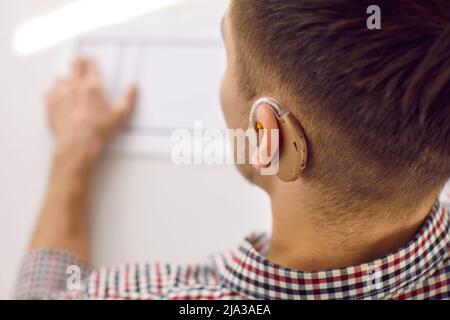 Close-up of modern model of hearing aid tucked into ear of unrecognizable young man. Stock Photo