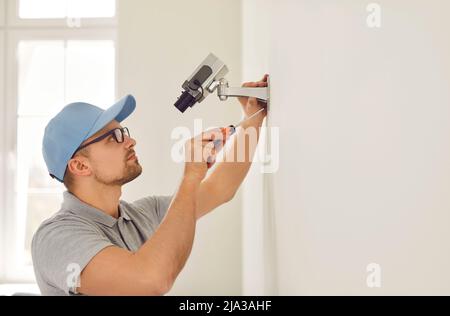 Professional male surveillance camera installer mounts it on wall inside new home or office. Stock Photo