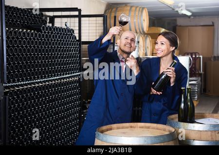 Two friendly winery workers holding glass of wine in aging section of factoryTwo friendly winery workers in aging section of factory Stock Photo