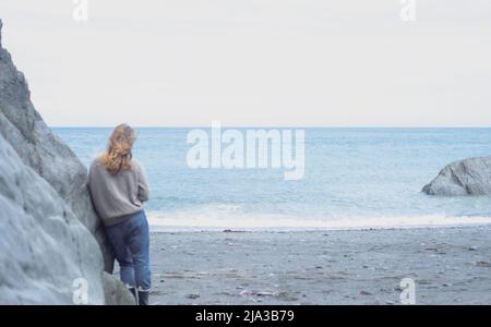 young woman gazing out to sea on Devon coastline. Stock Photo