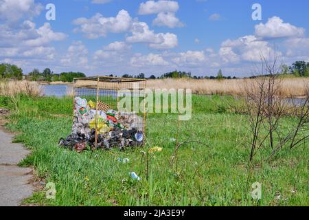 Overflowing dumpsters bank beautiful river and against background blue sky with clouds Stock Photo