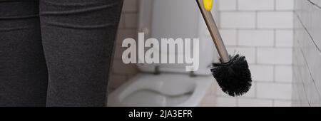 Woman in the toilet holding a brush for cleaning the toilet bowl Stock Photo