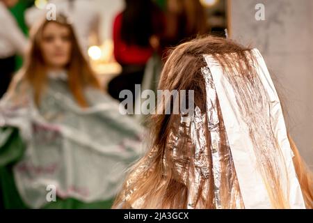 Beautiful young caucasian woman with foil in her hair while dyeing her hair sitting in a beauty salon Stock Photo