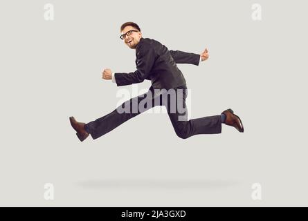 Crazy excited young businessman in black suit running and jumping isolated on gray background. Stock Photo