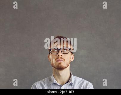 Young man with a questionable expression looks up while standing on a gray concrete background. Stock Photo