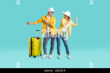 Positive young couple having fun and dancing going on summer trip isolated on light blue background. Stock Photo