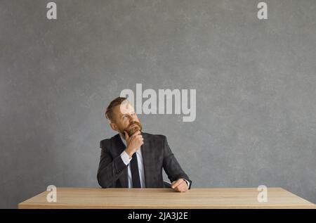Puzzled serious businessman with a pensive expression looks up holding his chin. Stock Photo