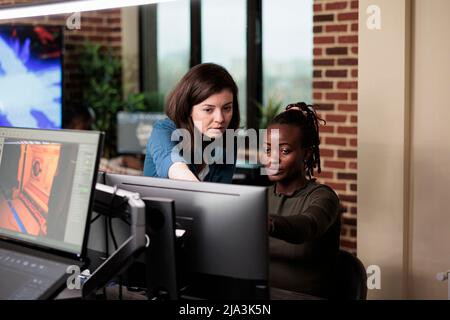 Company diverse employees discussing about development progress and electronic arts. 3D graphics designers in creative agency office workspace developing video game project. Stock Photo