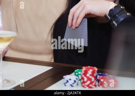 Women's hands shuffle cards. Concept of playing poker on the table with chips and cards. A glass of champagne. Gambling concept. Enjoying the moment, digital detox with friends. Selective focus. Stock Photo