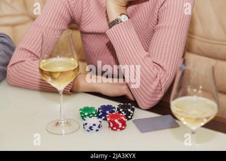 Women's hands close up. Concept of playing poker on the table with chips and cards. A glass of champagne. Gambling concept. Enjoying the moment, digital detox with friends. Selective focus. Stock Photo