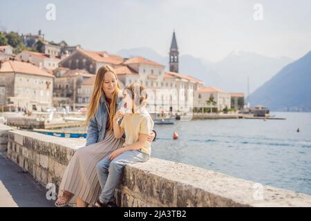 Mom and son tourists enjoying Colorful street in Old town of Perast on a sunny day, Montenegro. Travel to Montenegro concept. Scenic panorama view of Stock Photo