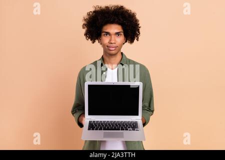 Portrait of attractive serious trendy wavy-haired guy holding laptop advert isolated over beige pastel color background Stock Photo