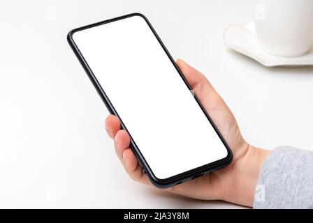 Mockup cellphone. female hand with cell phone with blank white screen on white table background. woman hand holding black cell phone smartphone with b Stock Photo