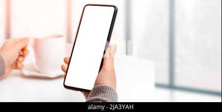 Mockup image of woman's hand holding black mobile phone with blank screen while drinking coffee. woman using cell phone mockup while drinking coffee i Stock Photo