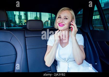 portrait of beautiful young successful blonde short haircut business woman with makeup in white business suit dress sitting on a leather chair works Stock Photo