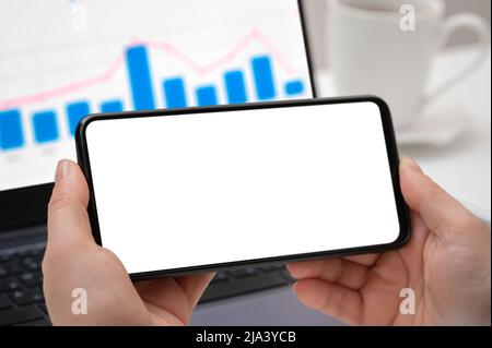 Mockup cellphone. Woman hand holding phone horizontally with blank screen in modern office close up view. businesswoman using smartphone horizontally Stock Photo