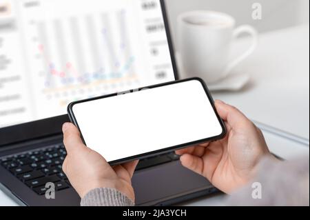 Mockup cellphone. Woman hand holding phone horizontally with blank screen in modern office. businesswoman using smartphone horizontally with blank scr Stock Photo