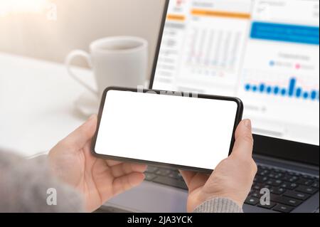 Mockup cellphone. Woman hand holding phone horizontally with blank screen in modern office. businesswoman using smartphone horizontally with blank scr Stock Photo