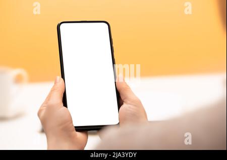 Mockup cellphone. hands of woman with cell phone against background of yellow wall and cup of coffee. Mockup image of hands holding mobile phone with Stock Photo
