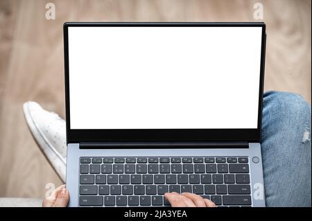 Top view mockup image of a woman working and typing on laptop computer with blank screen while sitting on sofa at home. Hand using laptop with blank w Stock Photo