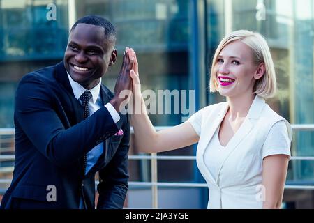 handsome African American businessman in a stylish black suit talking high five with attractive blonde woman business lady on the street background Stock Photo