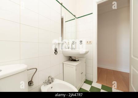 Bathroom with wooden furniture in white with porcelain sink, frameless mirror on the wall and white and green tiled floors Stock Photo