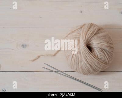 Aesthetic image of beige light, airy yarn skein. Medium thick blow yarn made of baby alpaca and merino wool on wooden background. Knitting needles stuck and skein of yarn. Copy space Stock Photo