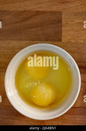 Two raw eggs with yellow yolks in white ramekin on wooden surface Stock Photo