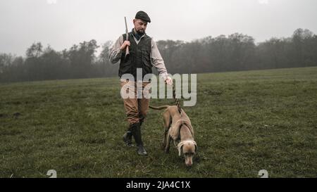 Hunter man with dog in traditional shooting clothes on field holding shotgun. Stock Photo