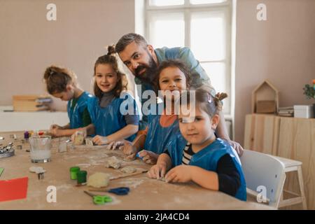 Group of little kids with teacher working with pottery clay during creative art and craft class at school. Stock Photo