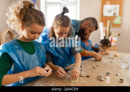 Group of little kids with teacher working with pottery clay during creative art and craft class at school. Stock Photo