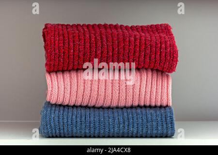 Stack of red, pink and blue wool cloth on shelf in white wardrobe Stock Photo