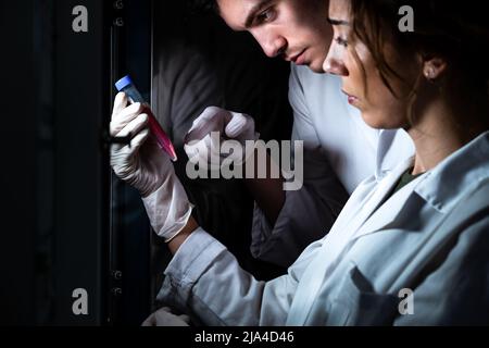 Close up of two scientist in lab coat holding and studying a medium tube with cells. Research, vaccine, health Stock Photo