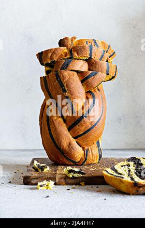 Unusual pumpkin marbled (tiger print) bread with cuttlefish ink, braided on a wooden board on a light background. Useful home baking. Stock Photo