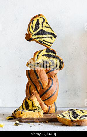 Unusual pumpkin marbled (tiger print) bread with cuttlefish ink, braided on a wooden board on a light background. Useful home baking, levitation. Stock Photo