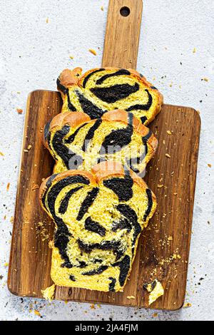 Unusual pumpkin marbled (tiger print) bread with cuttlefish ink, braided on a wooden board on a light background. Useful home baking. Stock Photo