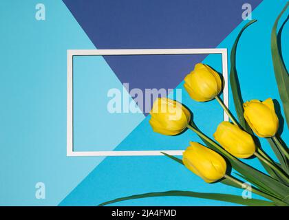 Nature composition with yellow tulips and paper card frame. Creative copy space layout made with spring flowers. Flat lay pastel blue background. Stock Photo