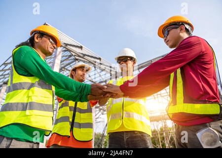 4 Workers in Construction Site, Architect and Engineer construction workers join hands while working at outdoors construction site. Building construct Stock Photo
