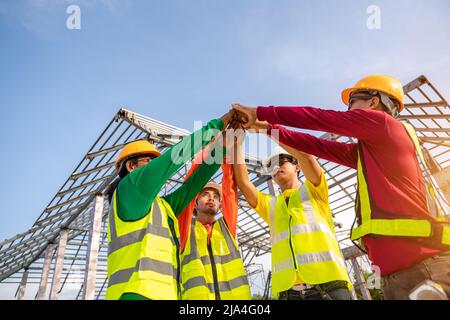 4 Workers, Architect and Engineer construction workers join hands while working at outdoors construction site. Teamwork Concept. Stock Photo