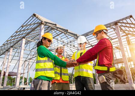 Architect and Engineer construction workers join hands while working at outdoors construction site. Teamwork Concept. Stock Photo