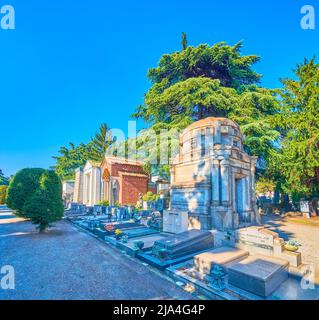 MILAN, ITALY - APRIL 5, 2022: The scenic funeral tombs along the shaddy alley in Monumental Cemetery, on April 5 in Milan, Italy Stock Photo