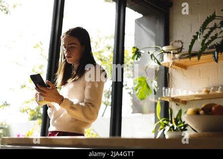 Thoughtful non-binary trans woman using smartphone near the window at home Stock Photo